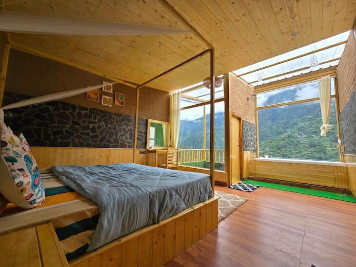 Glass House bedroom near Jibhi with a four-poster bed under a glass roof and the green valley through the window