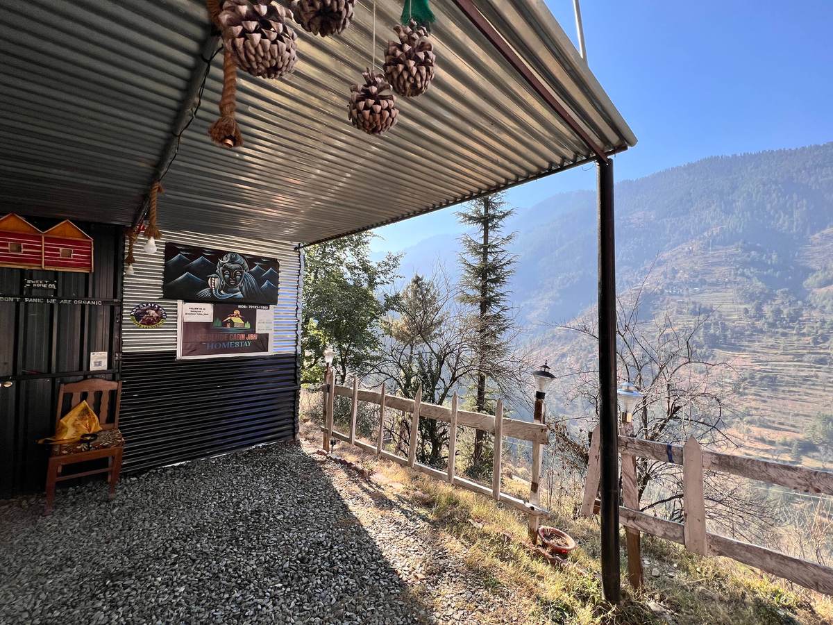 Covered wooden patio of the Mudhouse cottages with chairs and valley hillside beyond, Peaks N Valley Stays Chhet
