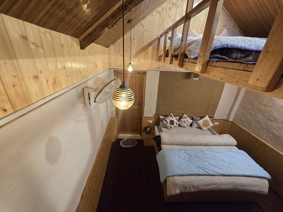 Inside a Mudhouse at Peaks N Valley Stays: a double bed below and a loft bed above under the wooden roof, Chhet near Jibhi